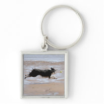 Dog chasing a ball at the beach key chain