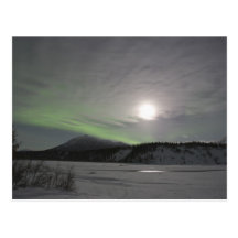 Moon rises over curtain of green aurora borealis postcard