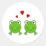 Two green frogs with red hearts. round sticker