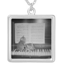 Two kittens sitting on piano keyboard by sheet necklace