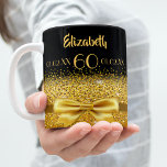 60th birthday gold bow black name age coffee mug<br><div class="desc">Elegant, classic, glamourous and feminine. A gold coloured ribbon and bow with golden glitter and sparkle, a bit of bling and everyday luxury. Black background. The Perfect gift for a 60th birthday! Templates for a name, age 60 and date of birth and the anniversary date. Golden letters. The name is...</div>