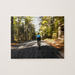 A female cyclist quickly rides on a small narrow jigsaw puzzle