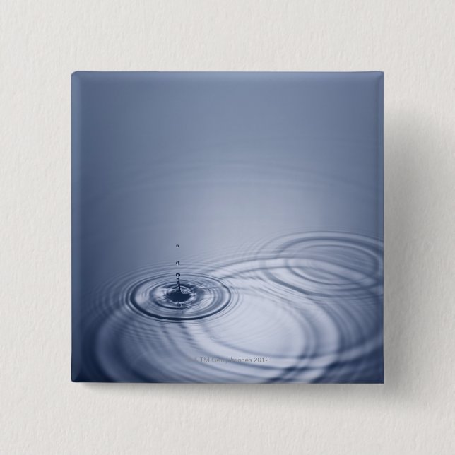 A single droplet of water falling into a calm 2 inch square button (Front)