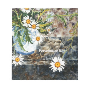 A white and blue pot of wild daisies on a shelf notepad