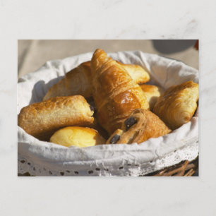 A wicker breakfast basket with croissants, and postcard