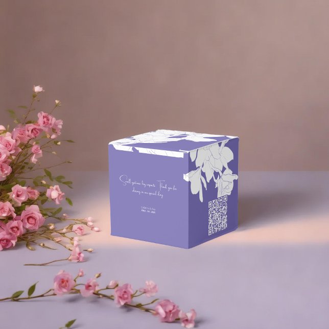 Ballotins Luxe violet fleuri (a purple floral favor box with a white flowers placed on soft surface surrounded with pnik flowers)