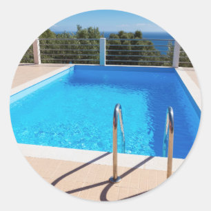 Blue swimming pool with steps at sea classic round sticker
