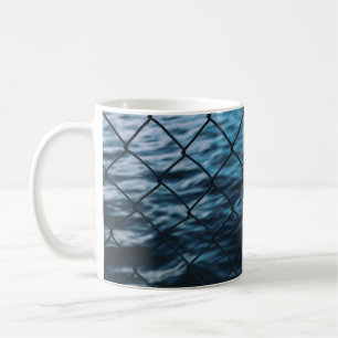 Body of water in front of chain link fence coffee mug