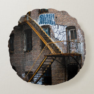BROWN BRICK BUILDING WITH YELLOW METAL LADDER ROUND PILLOW