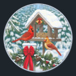 Cardinals and Christmas Bird Feeder Classic Round Sticker<br><div class="desc">A pair of Northern Red Cardinals perch on a snow-covered white picket fence adorned with Christmas garland and a bright red bow. They feast at a winter bird feeder decorated with Christmas bells,  ribbon,  and holly. Realistic Artwork created by wildlife artist Crista S. Forest.</div>
