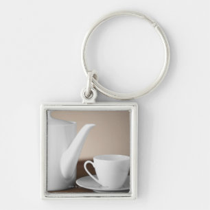 Close-up of a cup and a saucer with a tea kettle keychain