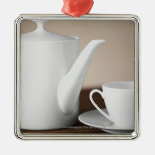 Close-up of a cup and a saucer with a tea kettle metal ornament
