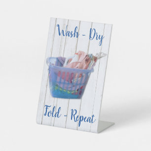 Colourful Folded Laundry On Hangers In Blue Basket Pedestal Sign
