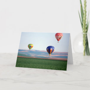 Colourful hot air balloons float over wheat holiday card