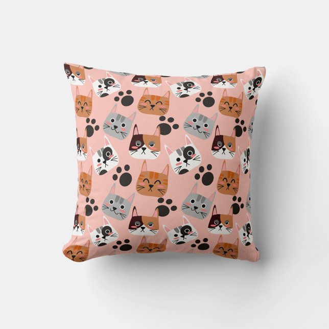 Coussin Faces de chat (A flat lay shot shows a square pillow with a pink background and a repeating pattern of cartoon cat.)