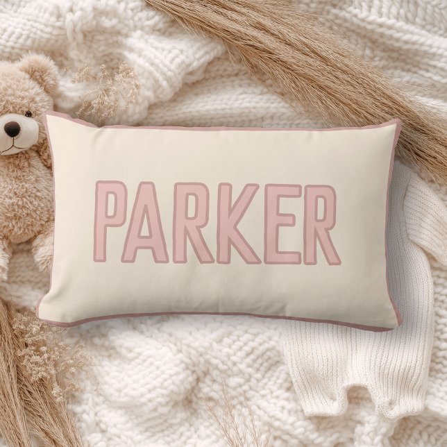 Coussin Rectangle Joli nom personnalisé pour enfants avec garniture  (A cream pillow with "WILDER" in light pink lettering lies on a cozy, soft-knit blanket)