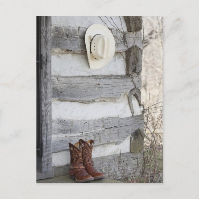 Cowboy boots and hat outside of log cabin postcard (Front)