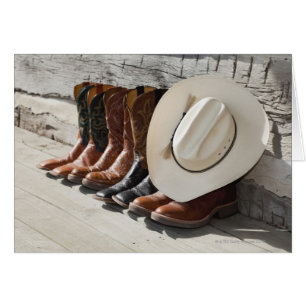 Cowboy hat on row of cowboy boots outside a log