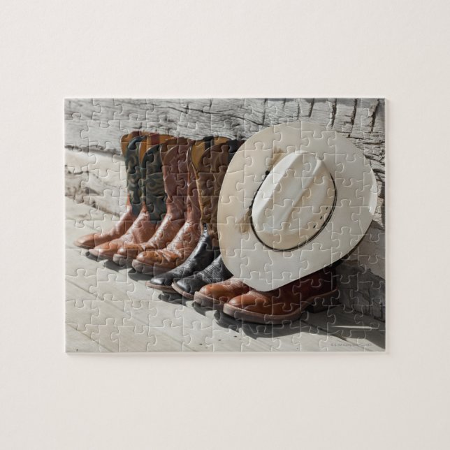 Cowboy hat on row of cowboy boots outside a log jigsaw puzzle (Horizontal)