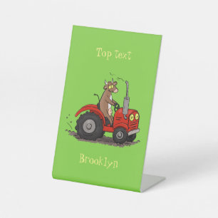 Cute happy cow driving a red tractor cartoon pedestal sign