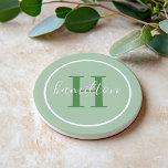 Elegant Sage Green Round Monogram Script Coaster<br><div class="desc">An elegant sandstone coaster featuring a leafy green serif initial and custom family name in script, framed by a white circle on a soft sage green background. The earthy, organic tones bring a calming, botanical warmth to any space. A beautiful personalized gift for housewarmings, garden lovers, or nature-inspired decor. All...</div>