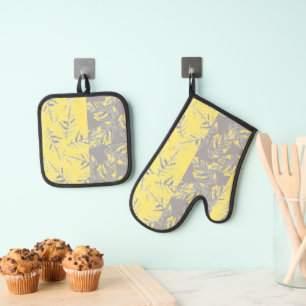 Ensemble De Gant De Cuisine Et De Manique Feuilles grises et jaunes sur un fond rayé.