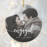 First Christmas Engaged Photo White Script Ceramic Ornament<br><div class="desc">Commemorate your engagement with this beautiful modern keepsake ornament. The white text reads "Our first Christmas engaged, " with the word "engaged" in bold handwriting script with flourishes before and after. Replace the sample image with your favourite photo, and add your names and the year. A dark gradient filter helps...</div>