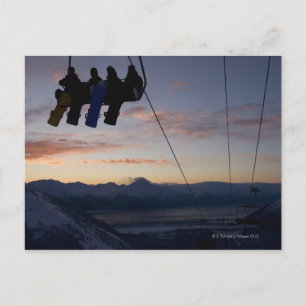 Four snowboarders are silhouetted on a ski lift postcard