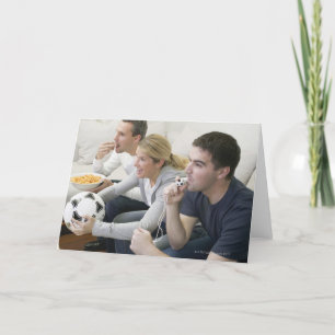 Friends watching TV with whistle, football and Card