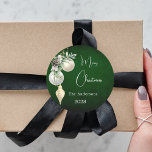 Green gold white baubles Christmas Classic Round Sticker<br><div class="desc">For a Christmas party favours or gift wrapping. A rustic green uneven coloured background. Decorated with white and gold baubles and some greenery and a pine cone.  Personalize and add your name,  year.  Text: Merry Christmas</div>