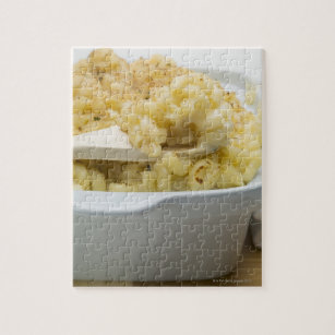 Macaroni cheese in baking dish with wooden jigsaw puzzle