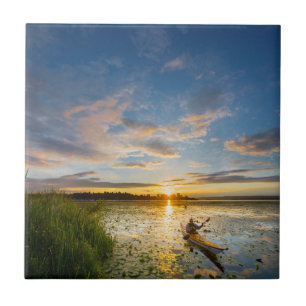 Male kayaker paddling sea kayak on still water tile