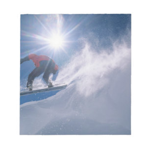 Man jumping off a large cornince on a snowboard notepad