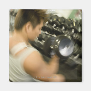 Man lifting dumbbell in gym, high angle view, magnet