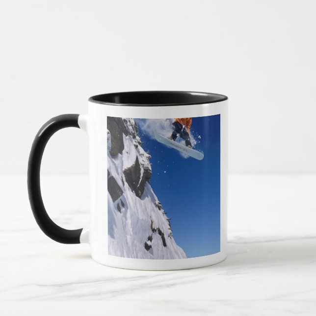 Man on a snowboard jumping off a cornice at mug (Left)