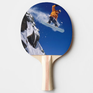 Man on a snowboard jumping off a cornice at ping pong paddle