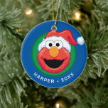 Merry Christmas Elmo Ceramic Ornament<br><div class="desc">Celebrate the holidays with a smile from everyone's favourite fuzzy red monster! This festive ornament features Elmo wearing a bright red Santa hat against a cheerful blue and green background. The ornament is fully customizable to include any name and the year making it an ideal personalized Christmas gift, yearly keepsake,...</div>
