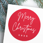 Merry Christmas handwritten script red Classic Round Sticker<br><div class="desc">Merry Christmas stickers with the text "Merry Christmas" in a handwritten style script font on a red background with the year or custom text below.</div>