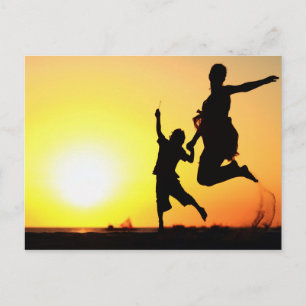 Mother and son silhouettes jumping on beach at sun postcard