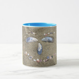 Mug yellow face made in the sand with sea shells