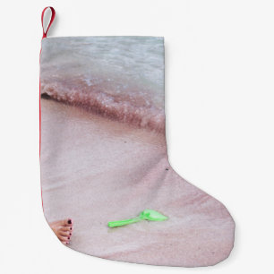 Person's foot beside green shovel on seashore small christmas stocking