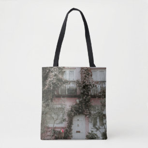 PINK AND WHITE PAINTED HOUSE COVERED WITH PLANTS A TOTE BAG