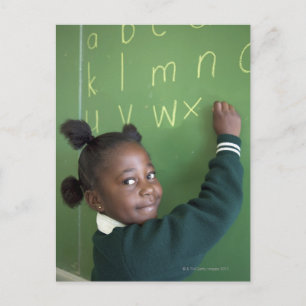 Portrait of smiling schoolgirl writing on the postcard