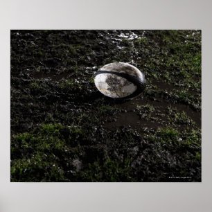 Poster Muddy rugby ball sitting on a chewed up grass