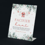 Red Christmas Santa Baby Pacifier Hunt Baby Shower Pedestal Sign<br><div class="desc">The Red Christmas Santa Baby Pacifier Hunt Baby Shower Game Sign adds a touch of holiday fun and excitement to your baby shower. Featuring a white background with festive red snowflakes, cheerful red berries, winter eucalyptus greenery, and Santa-themed baby clothes, this sign invites guests to join the "Pacifier Hunt" game....</div>