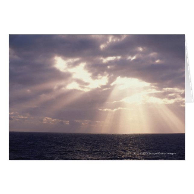 Setting sun shining through clouds over ocean (Front Horizontal)