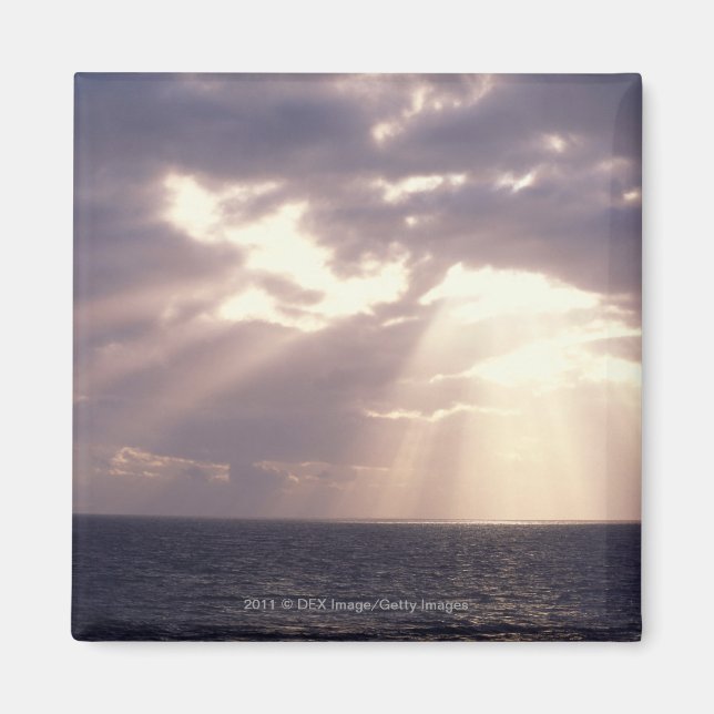 Setting sun shining through clouds over ocean magnet (Front)