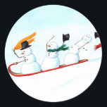 Snowmen on a Sled Classic Round Sticker<br><div class="desc">These three snowmen on a sled have been hand painted by Michelle Meyer and are racing down the snowy,  white hill. Two of them are having a great time while the third has already lost his hat and carrot nose,  and is trying desperately to hang on to his head!</div>