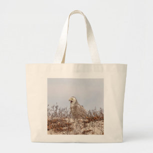 Snowy owl sitting on the beach large tote bag
