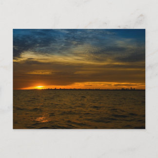 Sun setting down behind the city postcard